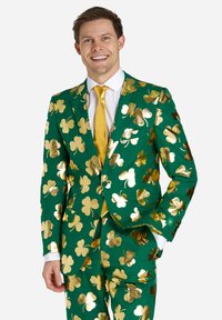 Zeleni sako z zlatim slamoškim vzorcem, z odrezanim ovratnikom, dvema gumboma in usklajenim zlatim šalom. Gladek material z sijočo površino.