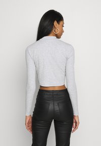 Top grigio corto a maniche lunghe realizzato in tessuto morbido, abbinato a pantaloni neri in pelle sintetica a vita alta con tasche e silhouette aderente.