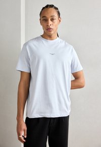 Ljusblå kortärmad t-shirt i mjuk bomull med rundad halsringning, prydd med liten svart text på bröstet. Matchad med svarta byxor.