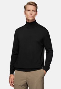 Black turtleneck sweater in a textured knit, featuring long sleeves and a fitted hem, paired with beige trousers.