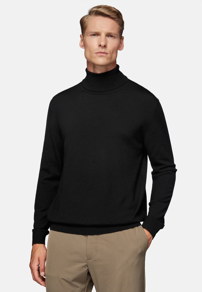Black turtleneck sweater in a textured knit, featuring long sleeves and a fitted hem, paired with beige trousers.
