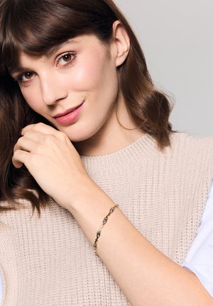 Złota skręcana bransoletka z czarnymi akcentami, o gładkim wykończeniu. Kobieta nosi ją na nadgarstku, podkreślając jej misterny wzór.