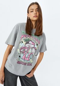 Camiseta de algodón gris con un diseño gráfico colorido que presenta setas, estrellas y flores. Mangas cortas, corte relajado y escote redondo.