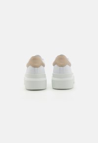 Valged sneakerid beeži kannatugedega, sile nahast ülajoon, tekstureeritud kummist tald ja platvormikujundus. Tagantvaade, mis näitab ümarat kuju.