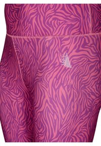 Fioletowe legginsy z wzorem zebry w różnych odcieniach, wykonane z elastycznego materiału, z widocznymi szwami i małym logo.