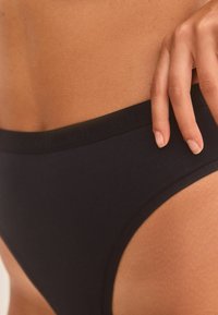 Zwarte katoenen bikini met een gladde textuur, voorzien van een subtiele elastische tailleband met merk en hoge beenuitsnijdingen.