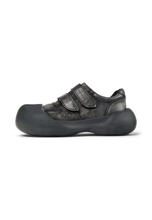 Schwarzer Ledersneaker mit einer übertrieben dicken Sohle und zwei breiten Klettverschlüssen oben, seitlich auf weißem Hintergrund gezeigt.