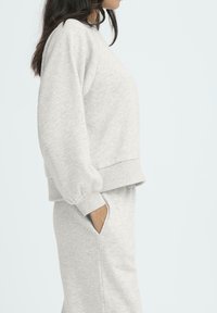 Sudadera gris texturizada con mangas abullonadas y puños acanalados, combinada con pantalones de chándal grises a juego que cuentan con bolsillos laterales. Ajuste casual.