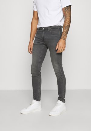 Slim-fit gray denim jeans with a slightly faded texture, paired with white sneakers and a plain white t-shirt. Features five pockets and a button closure.