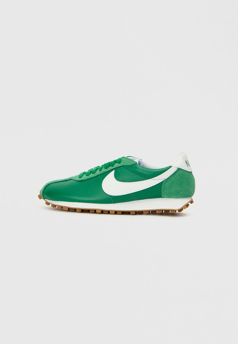 Sapatilha atlética verde com materiais de couro e camurça. Apresenta o logo da Nike em branco, bico redondo e uma sola de borracha texturizada para maior aderência.