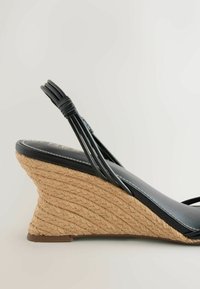 Sandale compensée en cuir noir avec talon plateforme en jute tressée et plusieurs fines brides autour du talon et du pied.