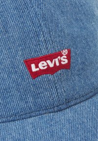 Gorra de mezclilla en azul claro con un logo bordado de Levi's en rojo y blanco en un panel frontal curvado. Presenta costuras a lo largo de los bordes.
