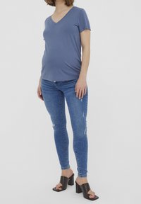 Camiseta azul de cuello en V con mangas cortas, combinada con jeans skinny claros desgastados y sandalias de tacón grueso negras.