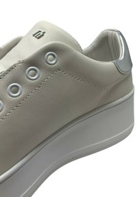 Sneaker in pelle crema con punta arrotondata, dettagli argentati sul tallone e sei fori circolari, montato su una suola bianca spessa.