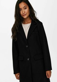 Black coat with a fitted design, two front pockets, and two button closures. Fabric has a smooth texture and structured lapel.