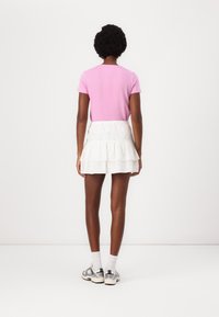 Pink short-sleeve shirt paired with a white tiered skirt featuring eyelet detailing. Footwear includes gray sneakers with white soles and socks.