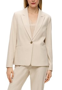 Beige op maat gemaakte blazer van textuurstof, met een enkele knoopsluiting, gesneden revers en twee zijzakken.