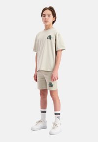 Lichtbeige katoenen t-shirt en shorts met een graphic print, gecombineerd met witte sneakers en gestreepte crew-sokken. Eenvoudig, casual ontwerp.
