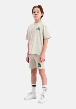 Lichtbeige katoenen t-shirt en shorts met een graphic print, gecombineerd met witte sneakers en gestreepte crew-sokken. Eenvoudig, casual ontwerp.