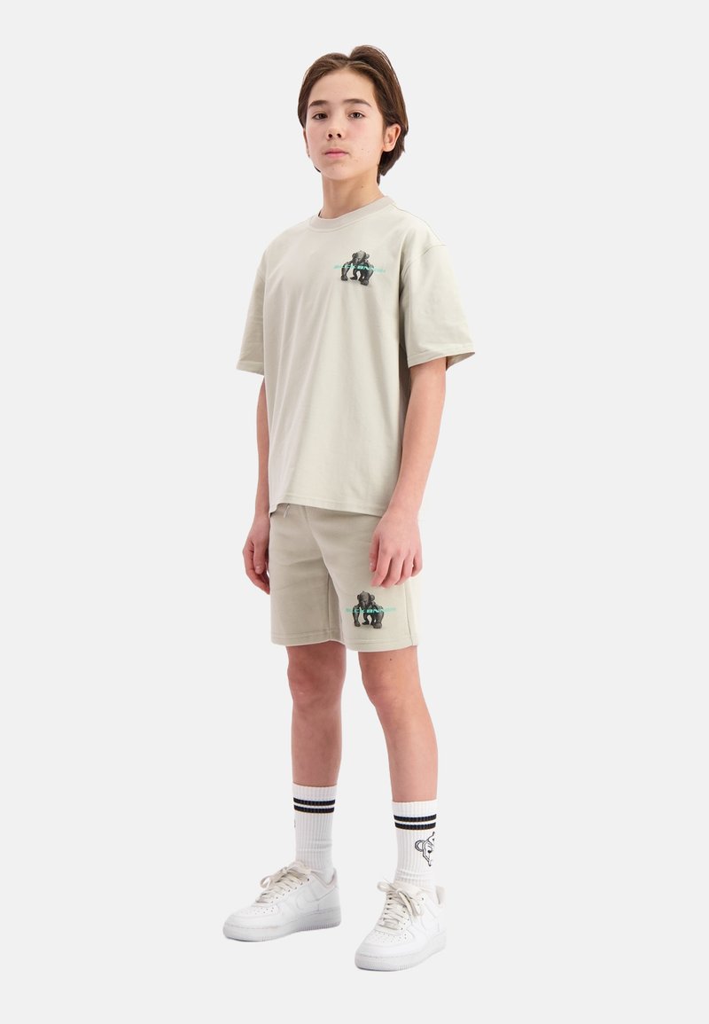 Lichtbeige katoenen t-shirt en shorts met een graphic print, gecombineerd met witte sneakers en gestreepte crew-sokken. Eenvoudig, casual ontwerp.