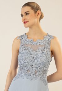 Helles blaues Kleid mit floraler Spitzenstickerei und Perlenakzenten, ärmelloses Design und nahtloser Übergang zu einem fließenden Rock.