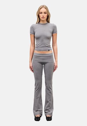 Femme debout, face à l'avant, portant un haut gris ajusté à manches courtes, un pantalon évasé assorti et des chaussures noires à bout fendu sur fond blanc.