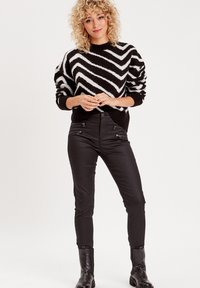 Pull à rayures noir et blanc avec une coupe décontractée et des poignets côtelés, associé à un jean skinny noir avec des accents zippés et des bottes chelsea.