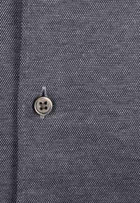 Donkergrijs geweven shirtstof met een klassieke knoop met vier gaten. De textuur toont een fijn, gelijkmatig patroon door het hele materiaal.