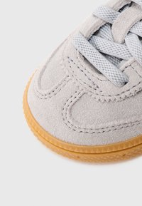 Svetlošedá semišová teniska s textúrovanými bočnými panelmi, svetlošedými šnúrkami a podrážkou z gumy s vzorovaným okrajom.