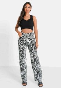 Czarny prążkowany crop top ze falbaniastym dekoltem, zestawiony z wysokim stanem szerokimi spodniami w czarno-białym wirującym wzorze.