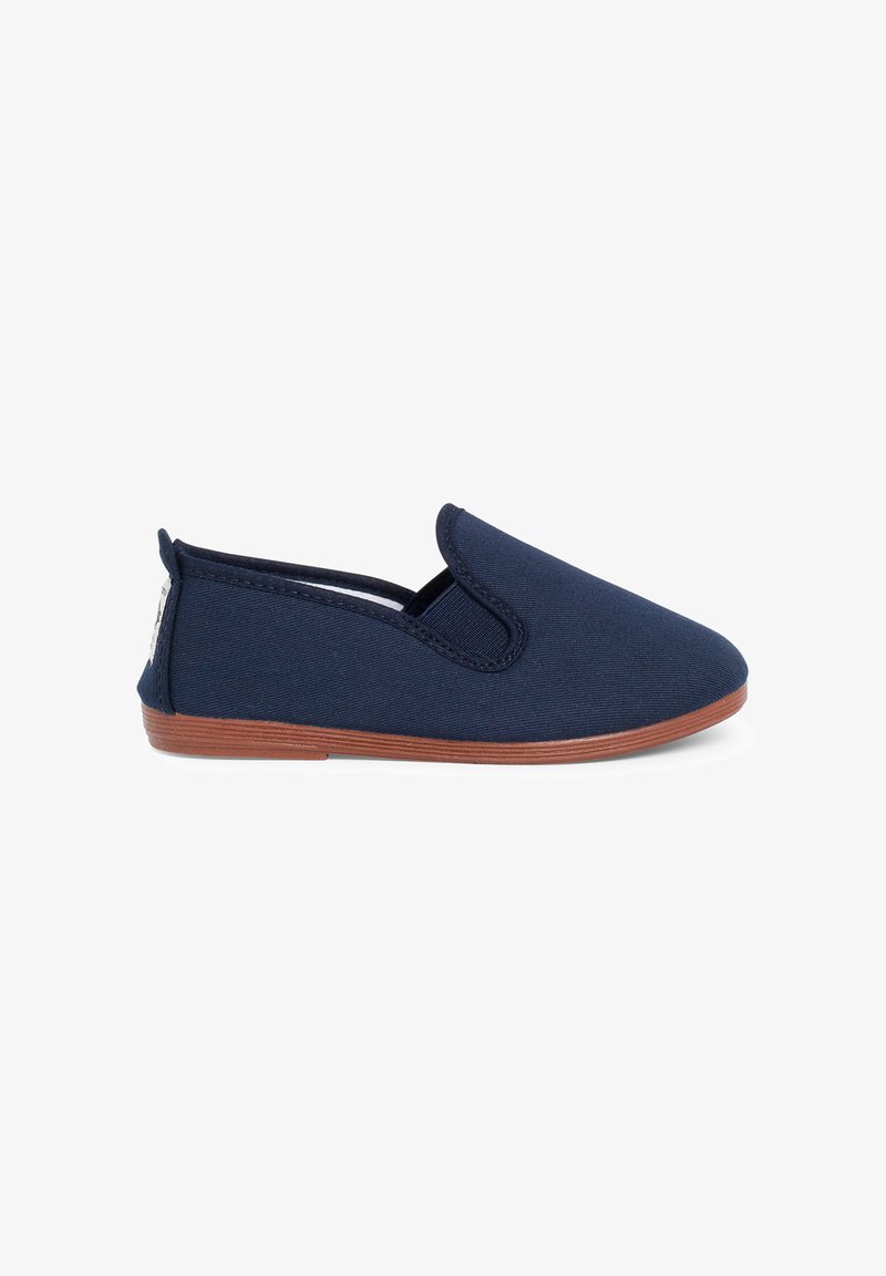 Zapato azul marino tipo slip-on con suela plana marrón, tacón bajo y paneles laterales elásticos para un fácil calzado.