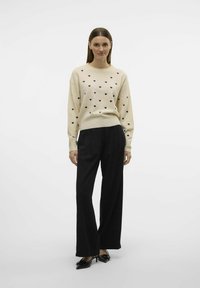 Pull crème avec des motifs de cœurs noirs, manches longues et ourlet côtelé. Associe avec un pantalon large noir et des chaussures noires à bout pointu.