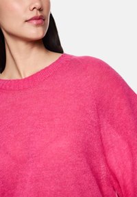 Fuchsia gestrickter Pullover mit geripptem Halsausschnitt und oversized Passform. Weicher Stoff mit leicht transparenter Optik.