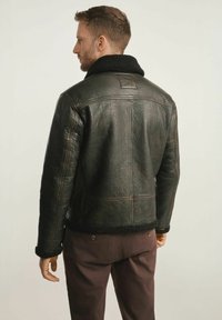 Czarna skórzana kurtka z fakturowanym wykończeniem, z kołnierzem z owczej wełny i brązowymi przeszyciami. Posiada skróconą sylwetkę oraz ściągacze przy mankietach.