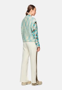 Knitted vest in blue and cream, layered over a patterned shirt with plaid and brown accents, paired with white pants and beige boots.