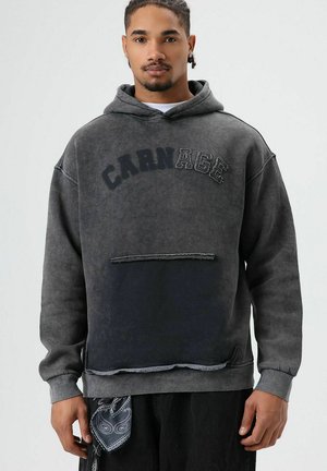 Sweat à capuche gris avec poche avant, ourlet usé, et grand texte "CARNAGE". Fabriqué en tissu doux et texturé avec des accents sombres.
