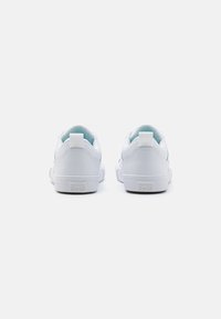 Zapatilla blanca con parte superior de cuero liso, suela de goma y interior azul claro. Presenta un pequeño logo en el talón. Diseño minimalista.