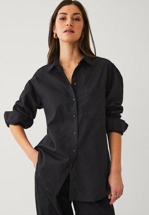 Schwarze Button-Down-Bluse aus leichtem Stoff, mit einer Brusttasche, hochgekrempelten Ärmeln und einem entspannten Schnitt. Glatte Textur und klassischer Kragen.