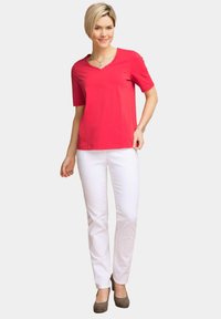 Rode T-shirt met korte mouwen en een V-hals, gecombineerd met witte straight-leg broeken en grijze hakken. Eenvoudig en modern outfitontwerp.