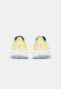 Vue arrière de chaussures de course en jaune et bleu clair. Présente un upper texturé, une semelle blanche et un logo "MACH 6" en rose.