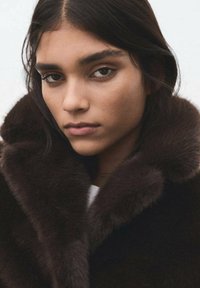 Bruine bontkraag om een model gewikkeld, met een zachte textuur en een luxe uitstraling, tegen een neutrale achtergrond.