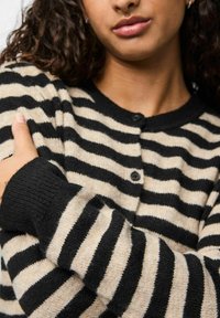 Randig kardigan i svart och beige, med rund halsringning, knappar, ribbade ärmslut och en mjuk textur. Ränderna växlar i bredd.