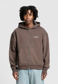 Brown zip-up hoodie with a spacious hood, kangaroo pockets, and ribbed cuffs. Features "RETERNITY" logo on the left chest.