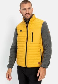 Quilted gul vest i gul med grå strikkede ærmer, med en lynlåslomme på brystet, sidelommer og et logo-patch på kanten.