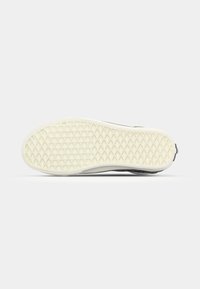 Semelle de chaussure avec un motif diamant et gaufré en blanc cassé, vue par le dessous sur un fond gris clair.