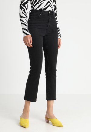 Jeans negros de talle alto con un ajuste slim y longitud recortada, hechos de tela vaquera, combinados con mules amarillos para un contraste.