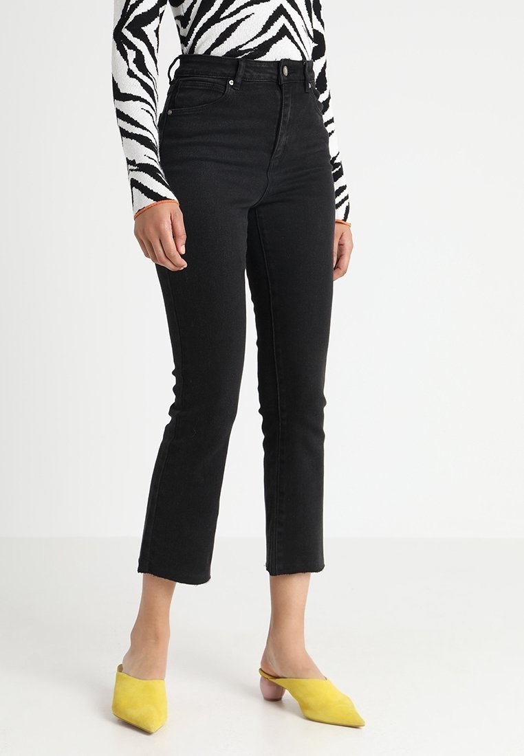 Höga svarta jeans med smal passform och kort längd, tillverkade av denimtyg, ihop med gula klackar för kontrast.