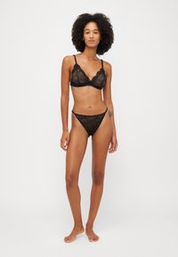 Sorte blondet undertøysett med en bralette med blomstermønstre, justerbare stropper, og en matchende blondet thong. Glatt, transparent tekstur.