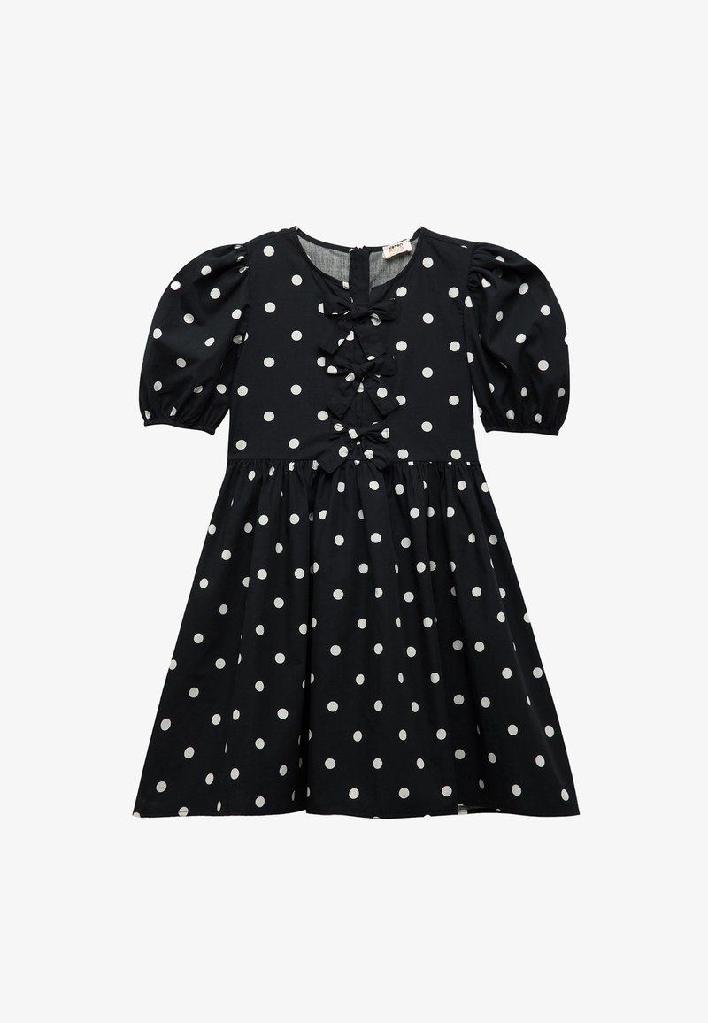 Musta mekko valkoisilla pilkuilla, lyhyet puffhihoilla, V-pääntie ja koristeelliset frillat etupuolella. Laajeneva hameen muoto.