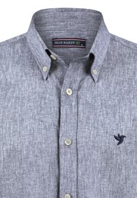 Camisa de manga larga gris con tejido texturizado, que presenta un pequeño logo bordado de un pájaro en el lado izquierdo del pecho y botones beige.